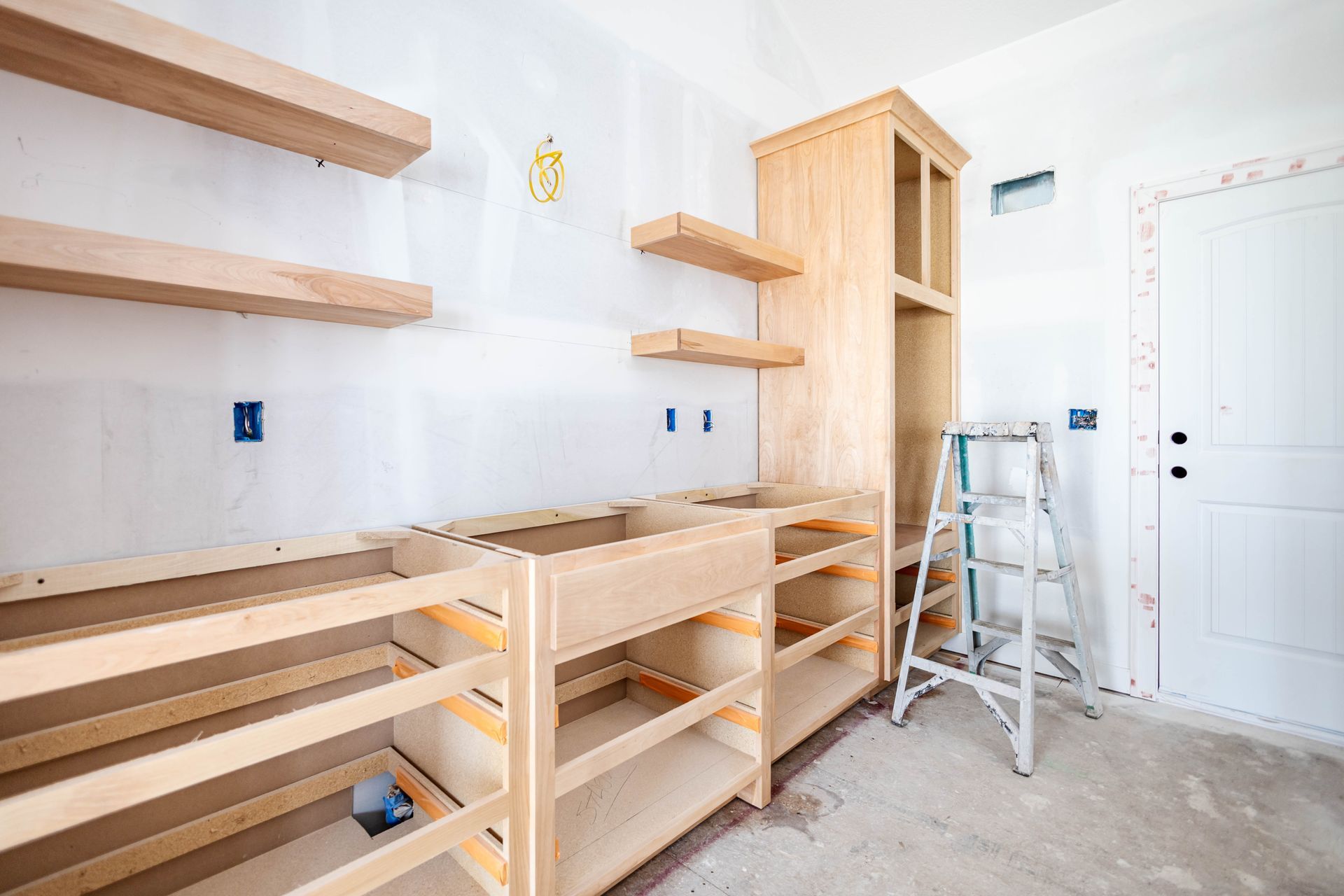 Unfinished kitchen with exposed cabinets, shelves, and a cabinet, against a white wall.