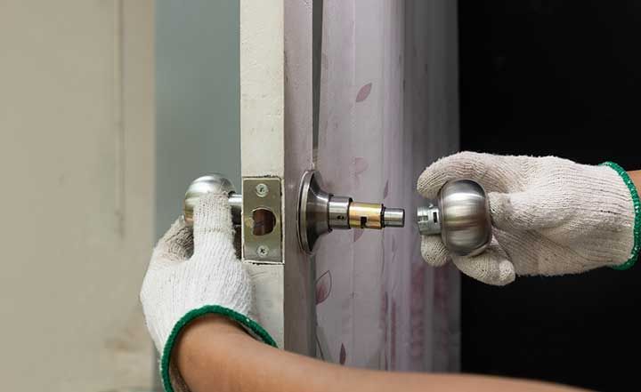 Locksmith on wood door with screwdriver for repair or fix silver knob.