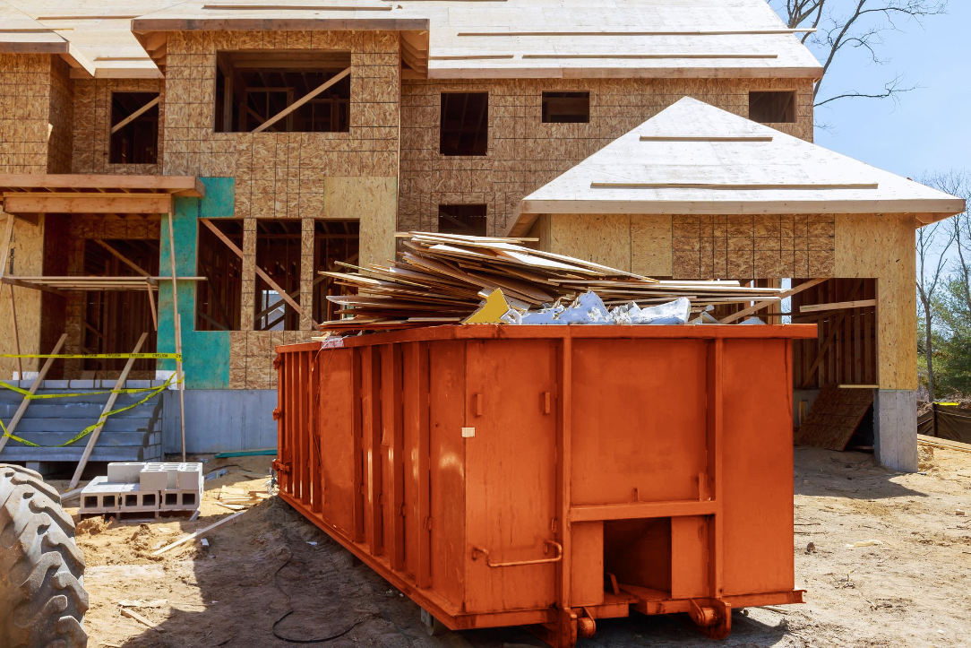 A large orange dumpster is parked in front of a house under construction.