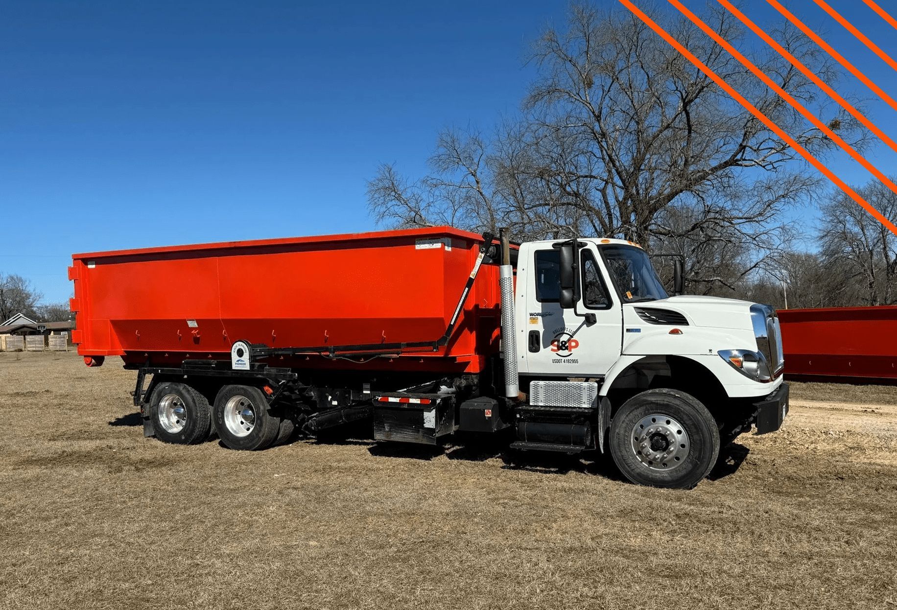 A dump truck is parked in a field with trees in the background.