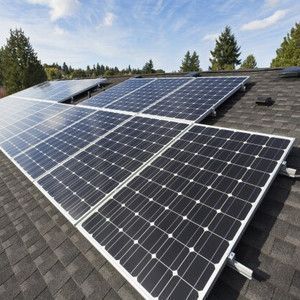 Solar panels installed on a dark rooftop under a blue sky.