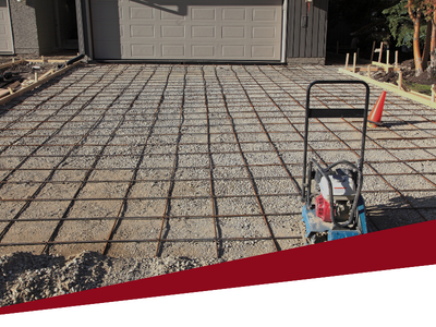 Freshly poured concrete driveway with a square grid pattern in front of a garage, with a tool cart at right.