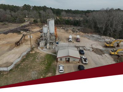 Aerial view of a construction site with heavy machinery, concrete plant, and trucks on a dirt lot.