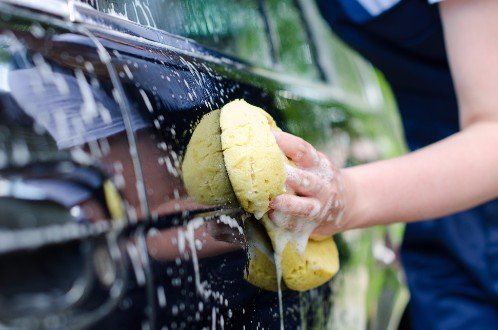 mani di una donna che lavano con una spugna la carrozzeria della macchina