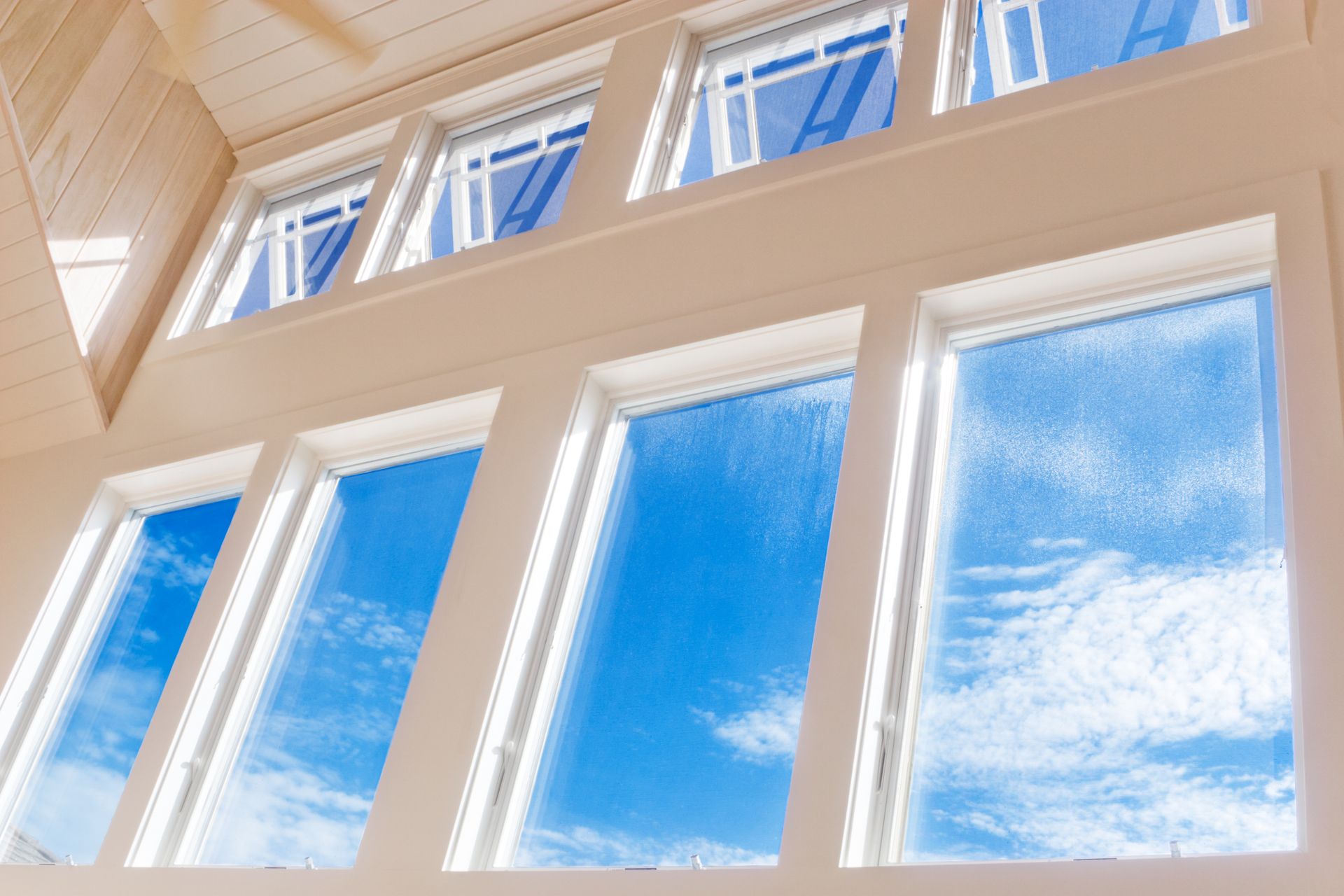 Tall white-framed windows looking up to a bright blue sky with clouds. Tall white-framed windows looking up to a bright blue sky with clouds.