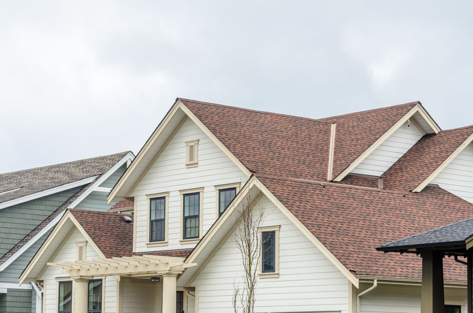 Row of suburban houses with cream siding and red shingle roofs under a cloudy sky Row of suburban houses with cream siding and red shingle roofs under a cloudy sky