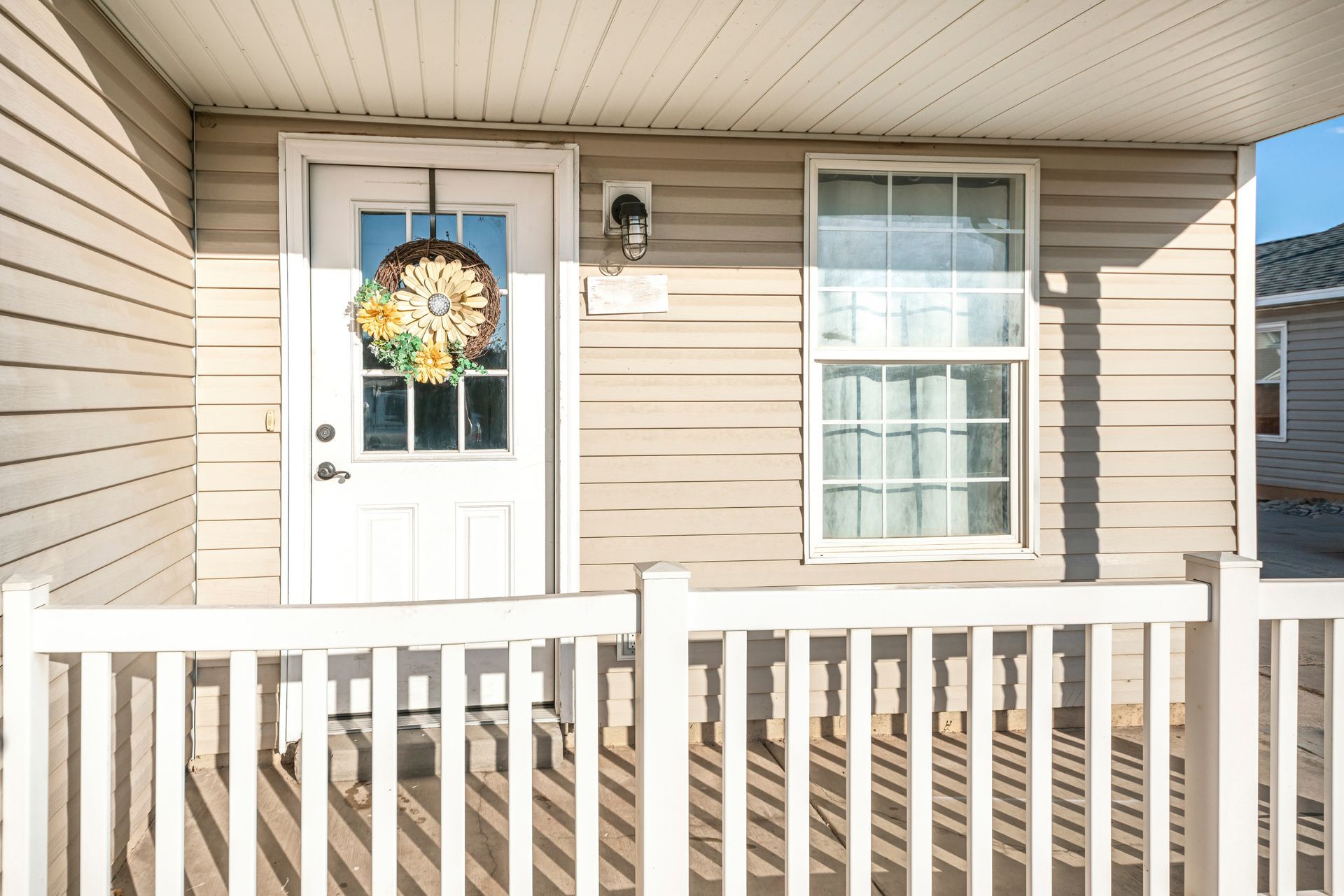 Front porch with white railing, beige siding, white door with wreath, and a window. Front porch with white railing, beige siding, white door with wreath, and a window.