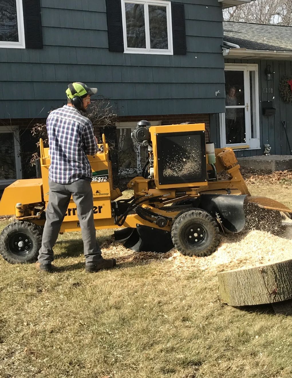 A man is standing next to a stump grinder in front of a house.