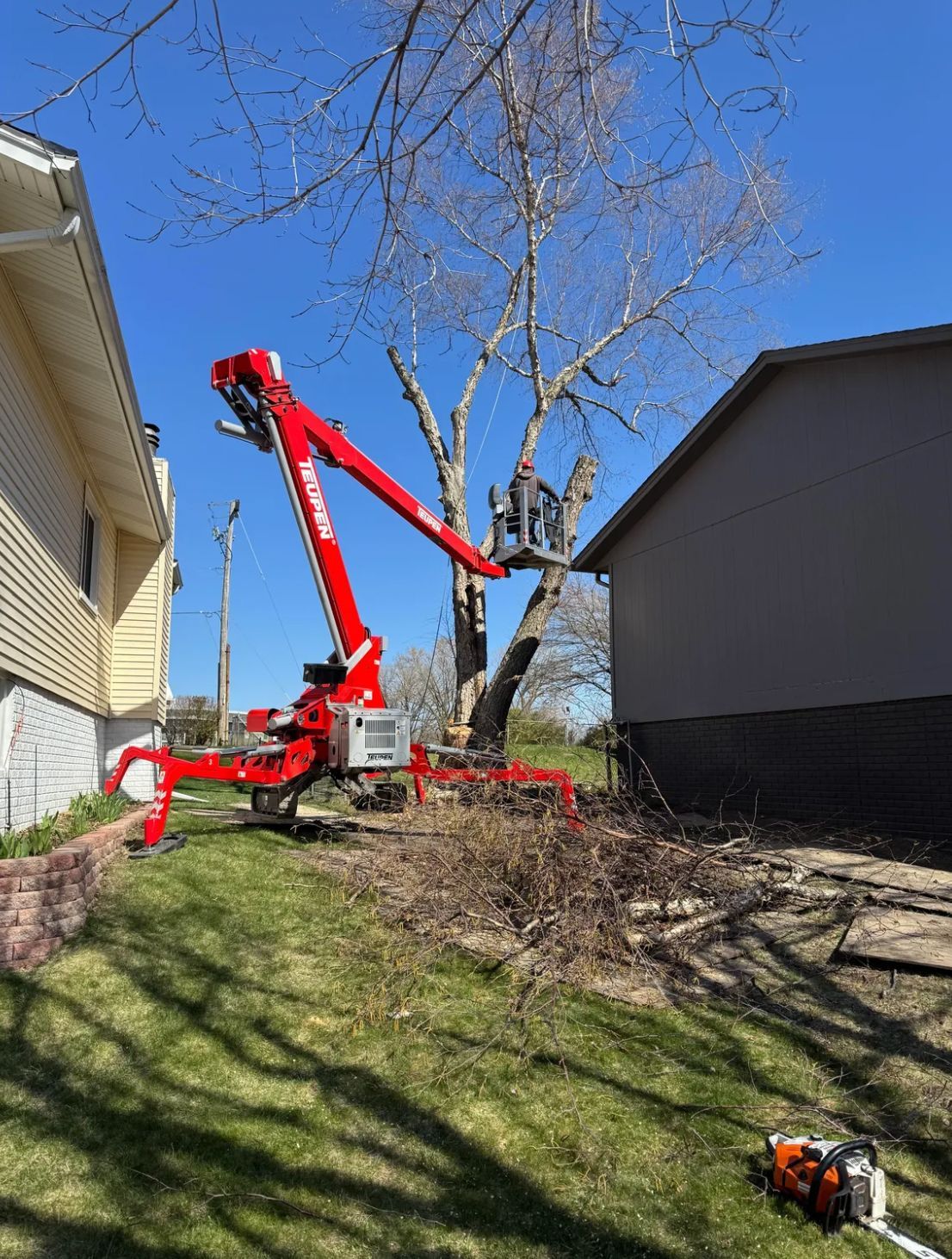 A red crane is cutting a tree in front of a house.