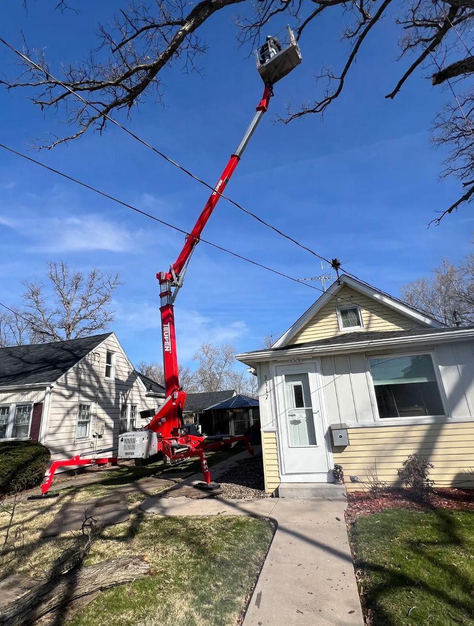 A crane is lifting a tree in front of a house.
