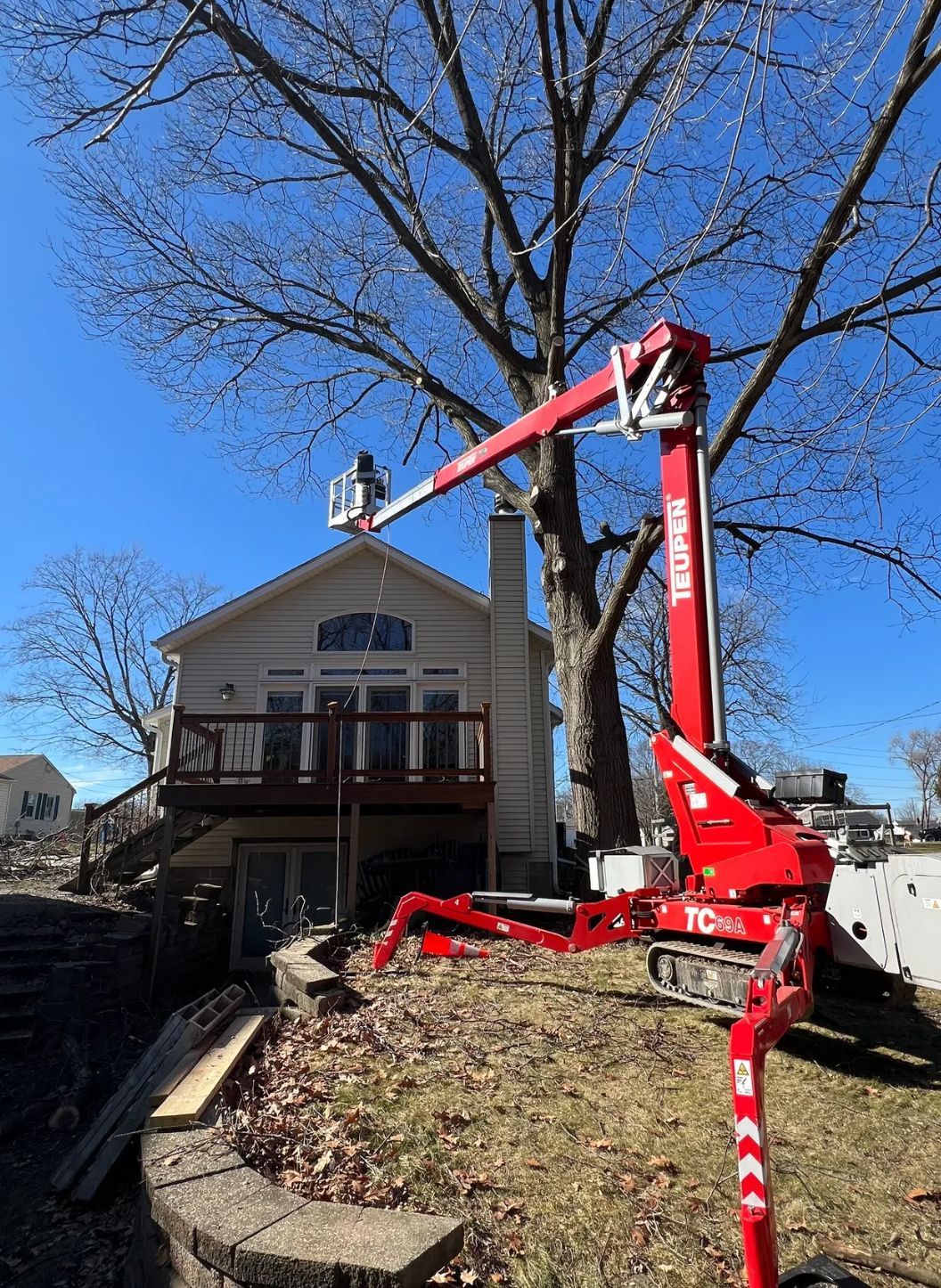 A red crane is cutting a tree in front of a house.