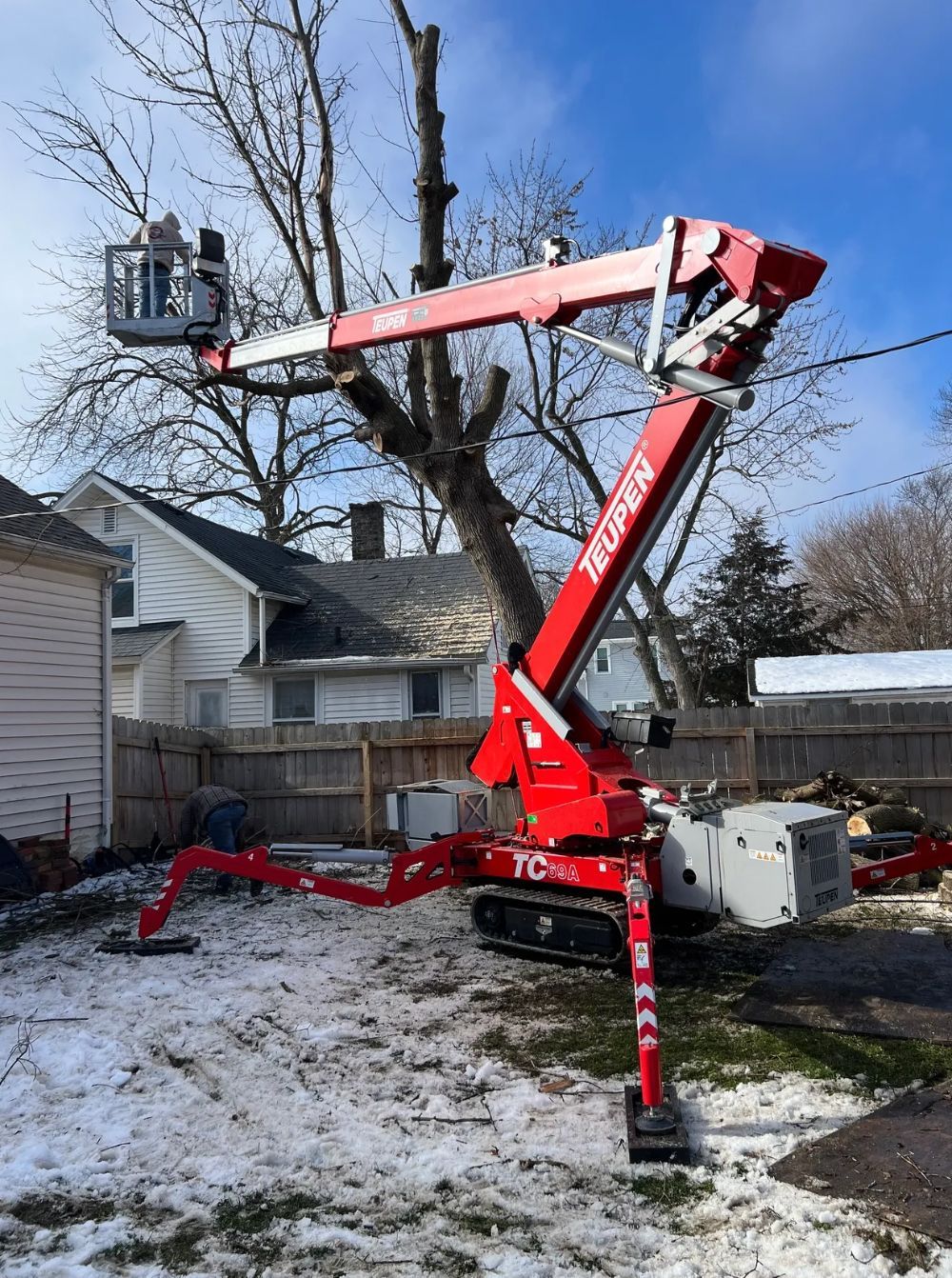 A red crane is cutting a tree in front of a house.
