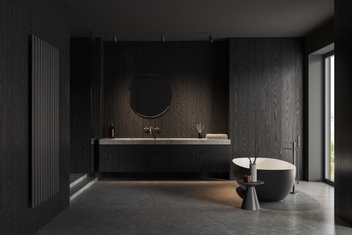 A minimalist, modern bathroom with dark wood walls, a round mirror over a floating vanity, and a freestanding tub.