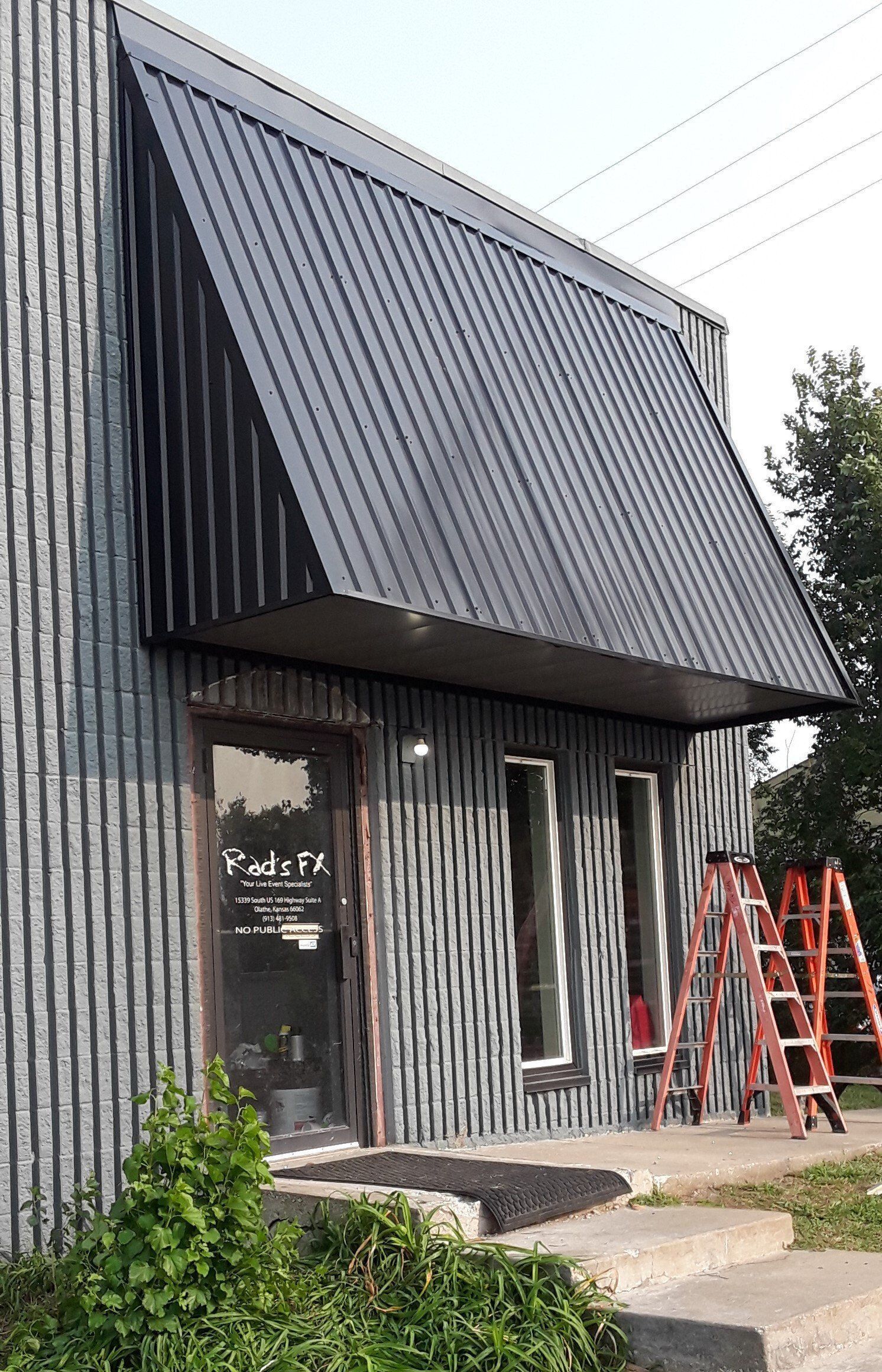 Small gray corrugated building with a steep black awning and ladders outside