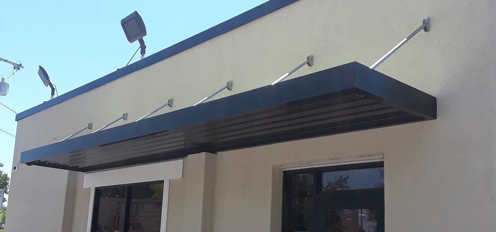 Blue awning over a beige building entrance with dark windows under a clear sky