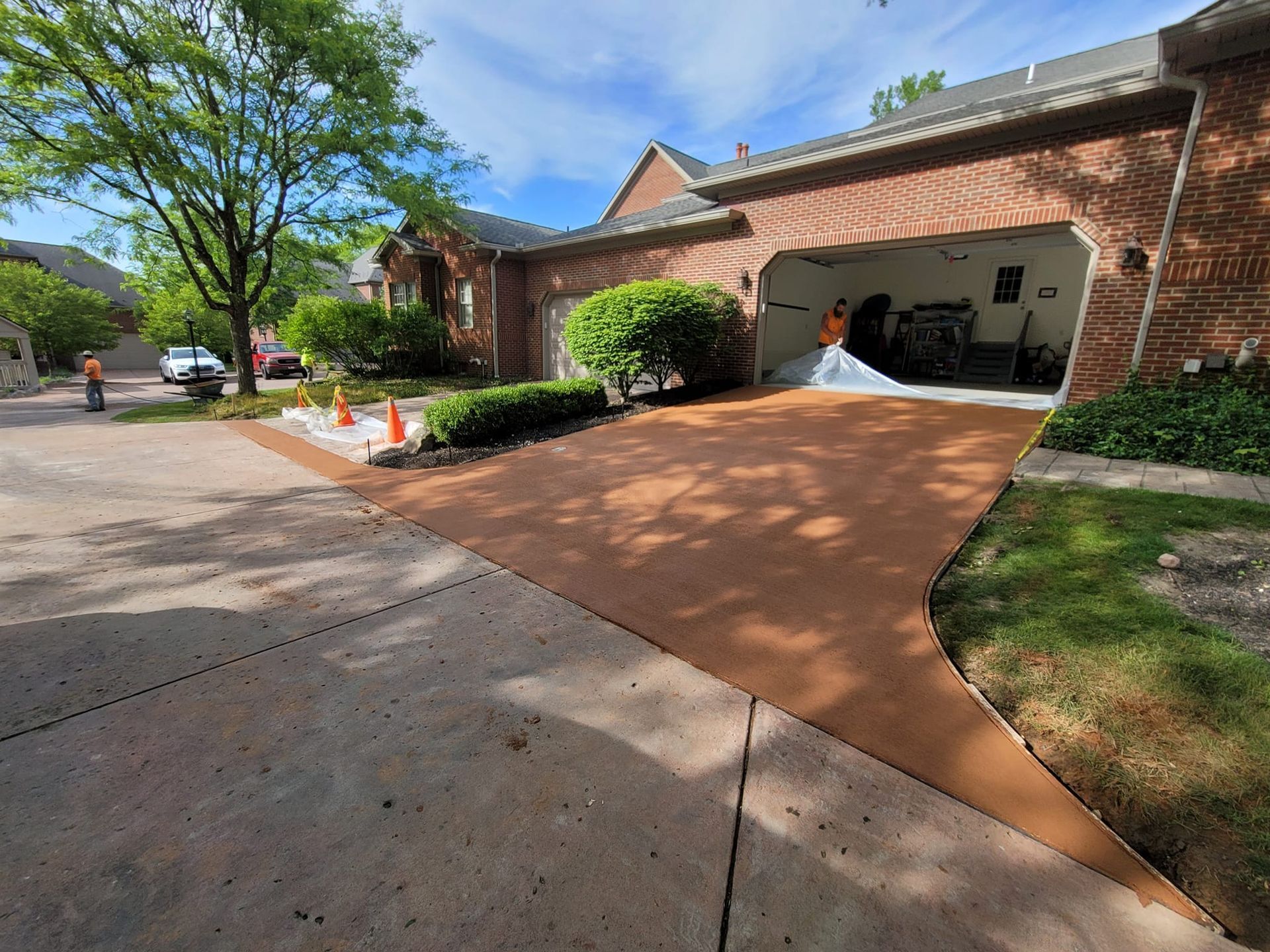 Brown coated driveway leading to a brick garage. Orange cones line the edge.