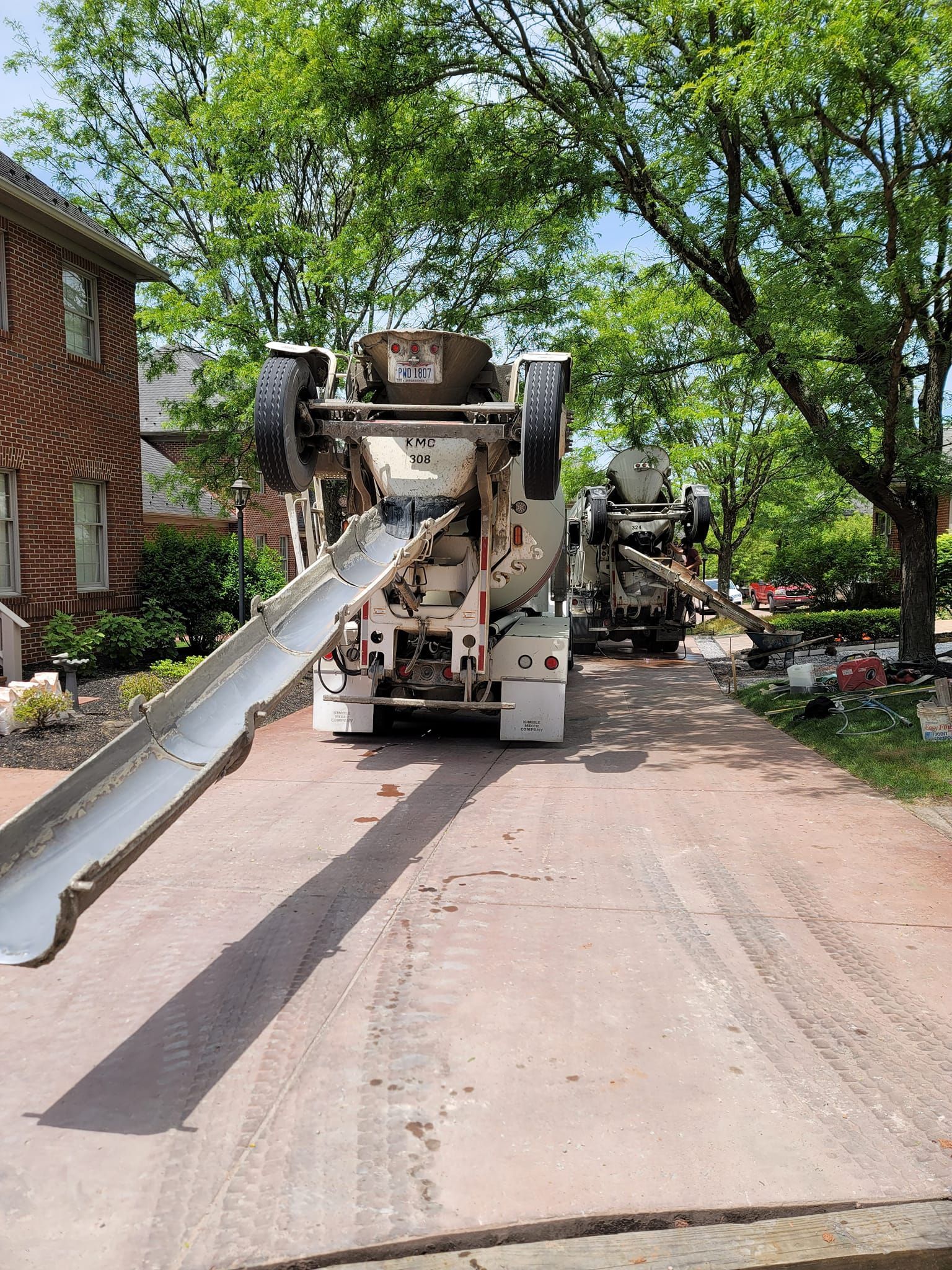 Concrete truck pouring concrete on a driveway, trees and brick house in the background.
