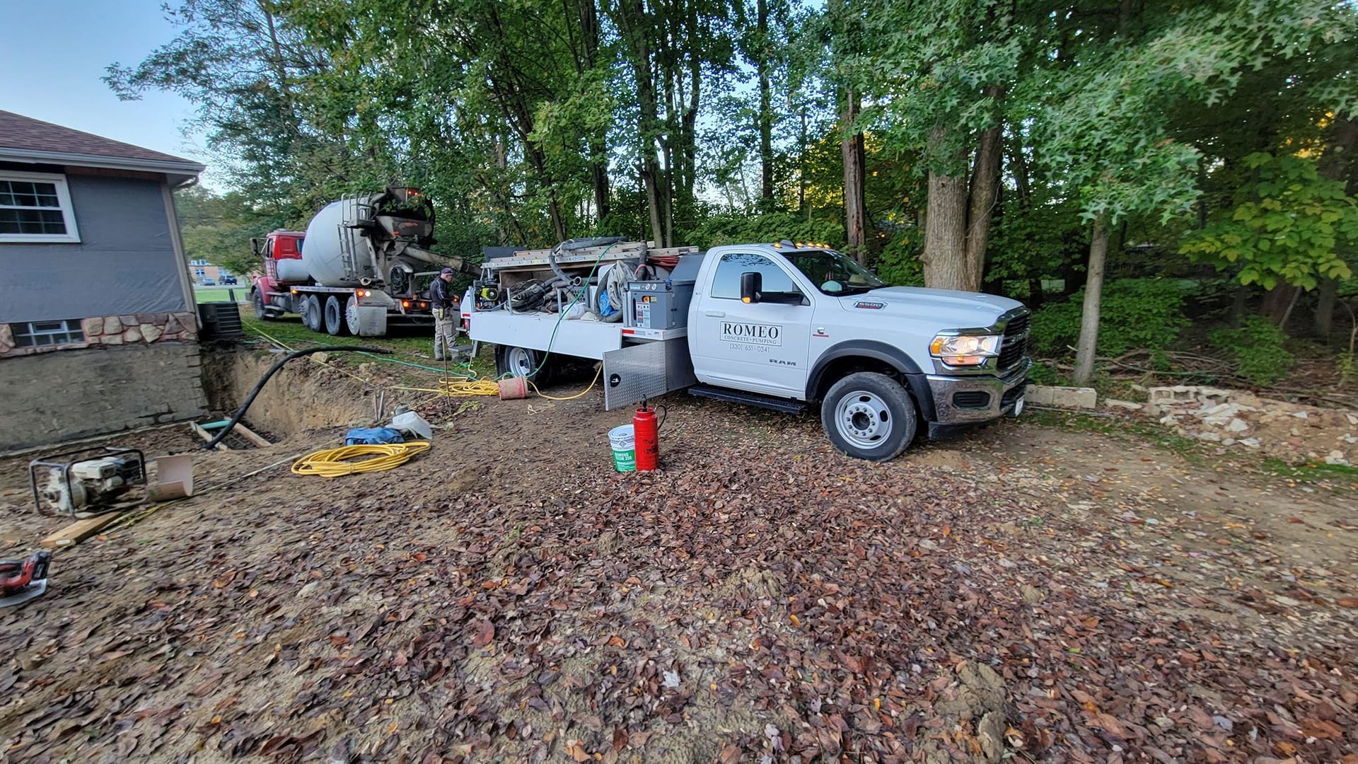 White truck parked near house with concrete truck in the background, likely a construction site.