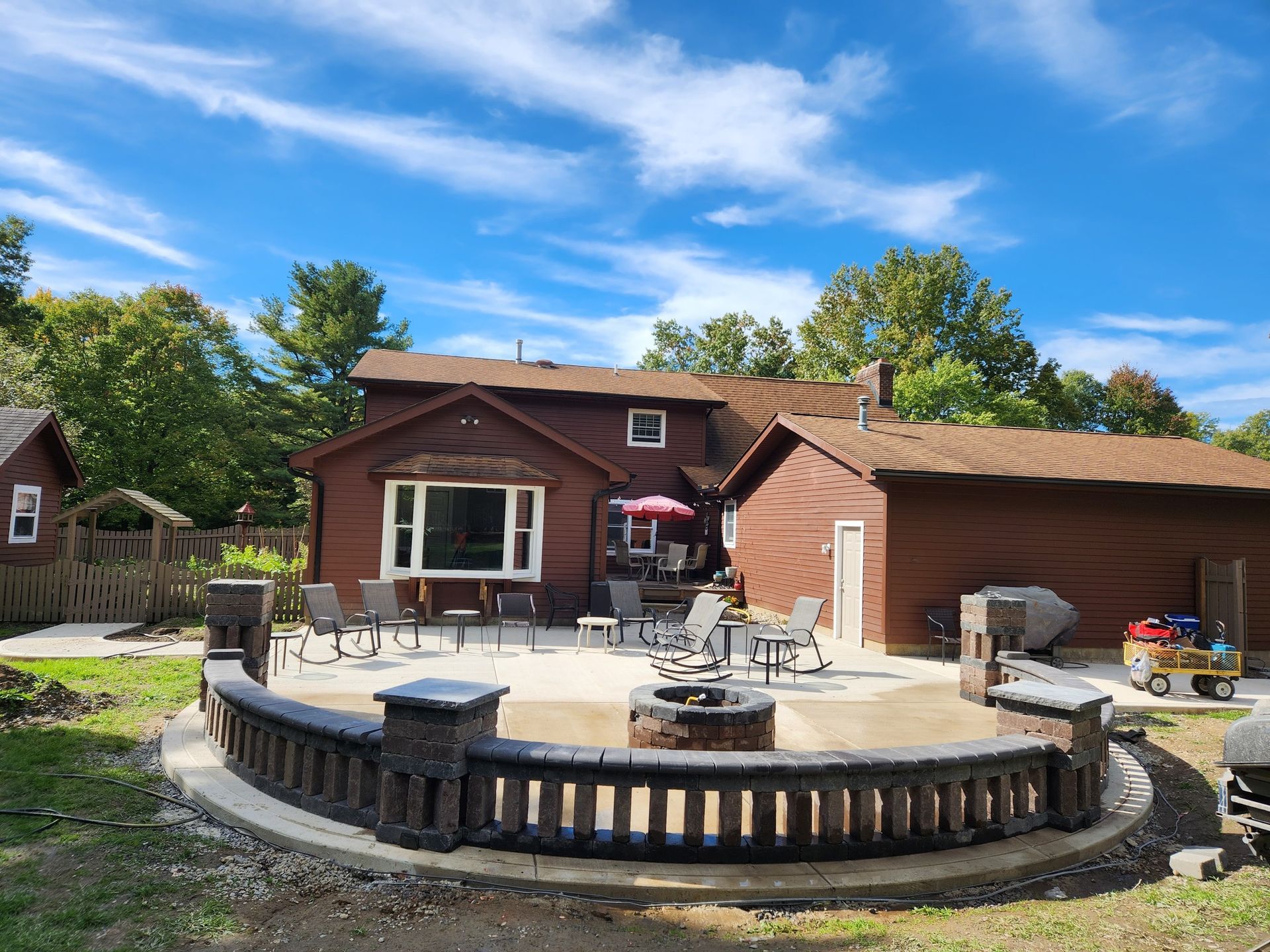 Backyard patio with fire pit, seating, and a brown house on a sunny day.