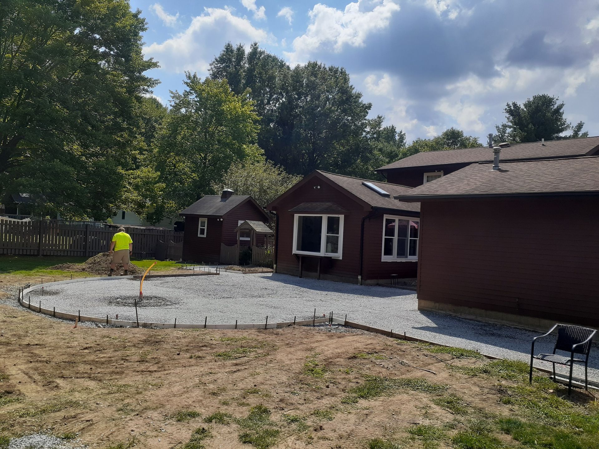 Backyard with gravel patio, small buildings, and a person in a yellow vest.