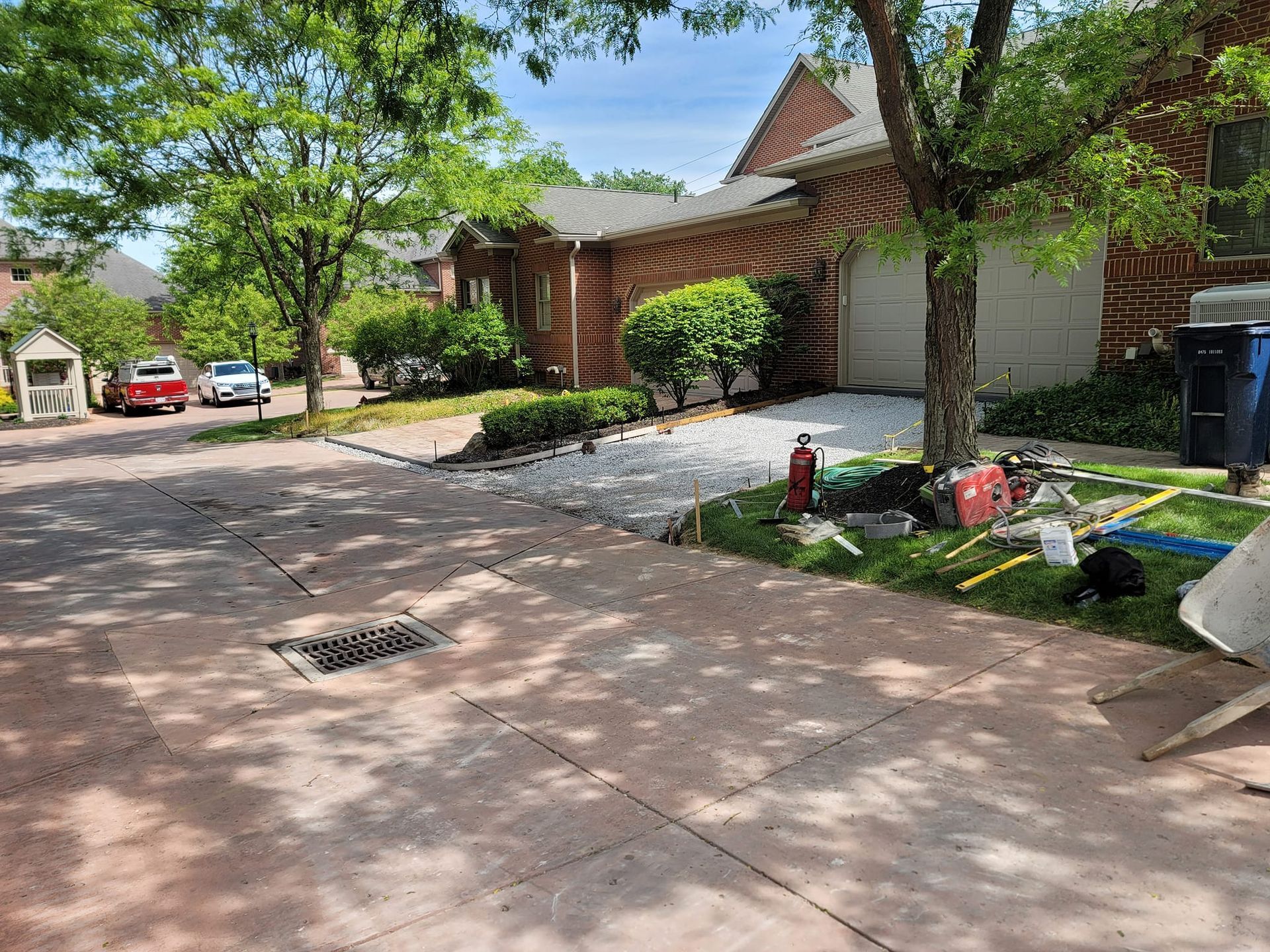 Driveway under construction in front of a house, with exposed gravel and construction tools visible.