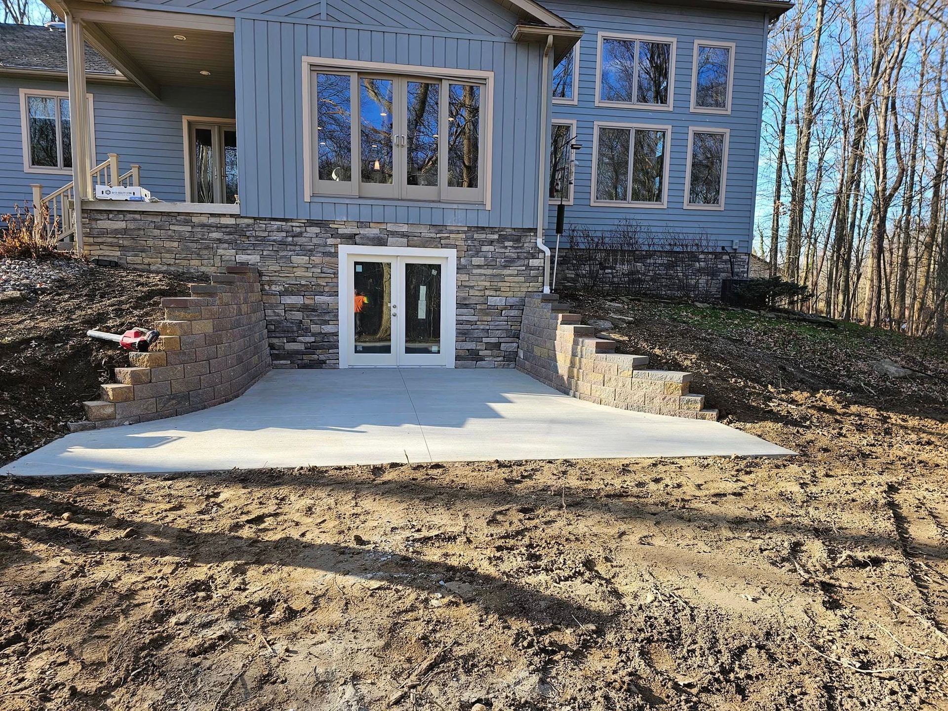 A house with a concrete patio, stone retaining walls, and steps leading to a yard.