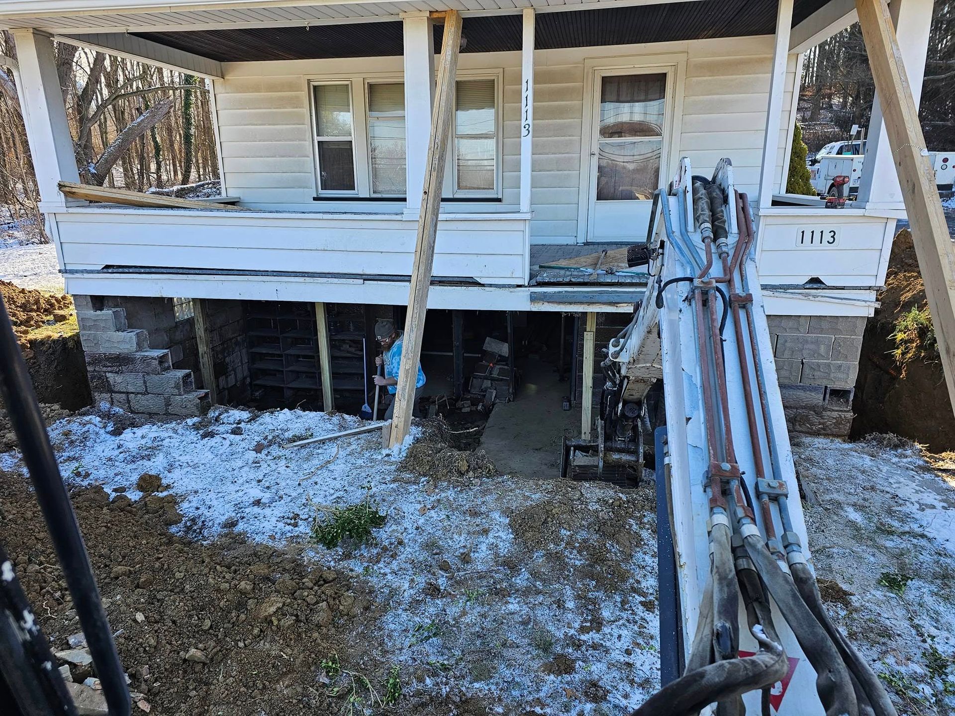 House undergoing foundation work, supported by wood beams, outdoor setting with snow.