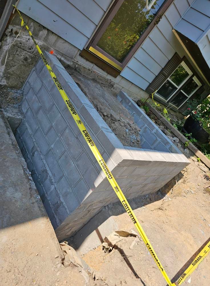 Concrete block retaining wall under construction next to a house with caution tape.