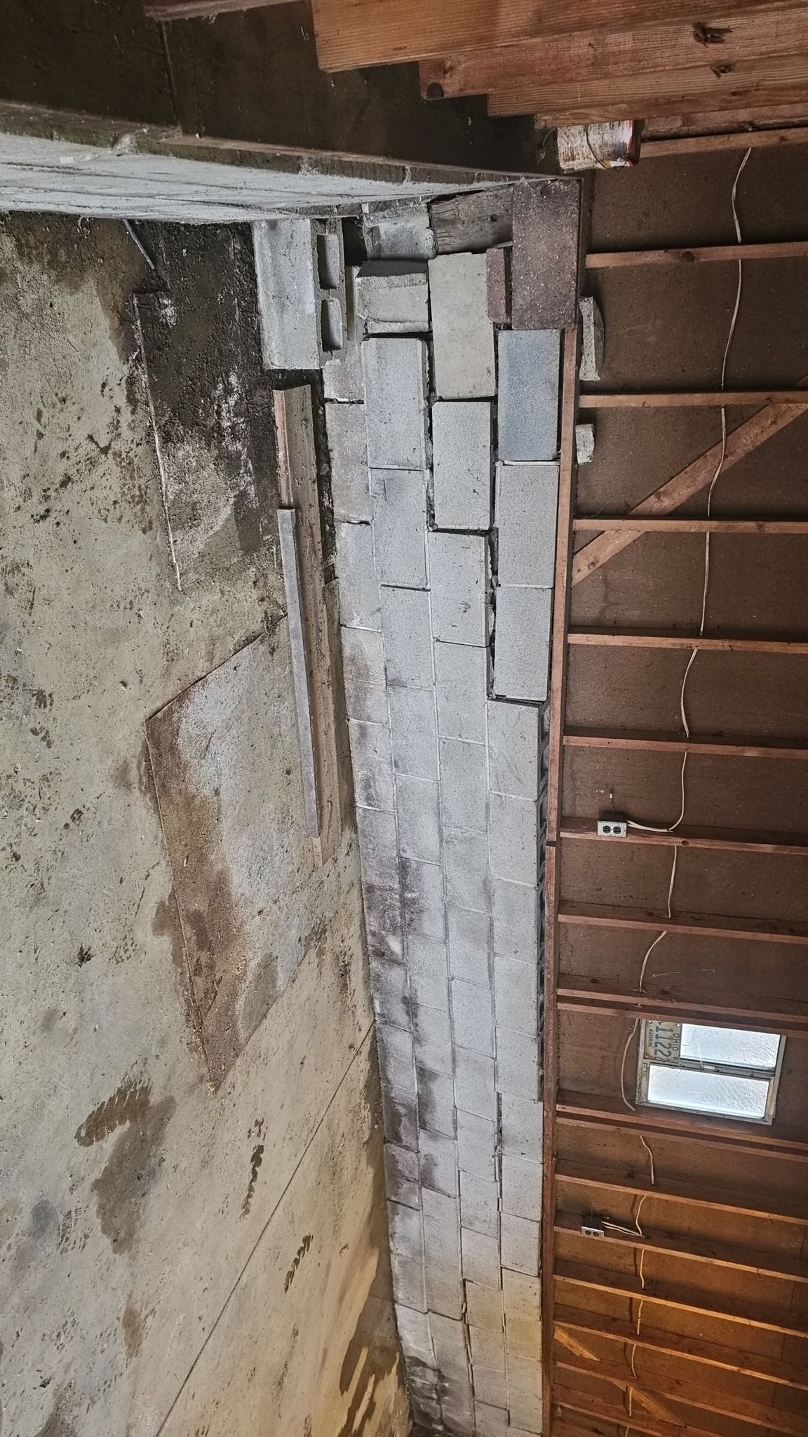 Brick wall and wooden rafters in an unfinished structure, with a small window visible.