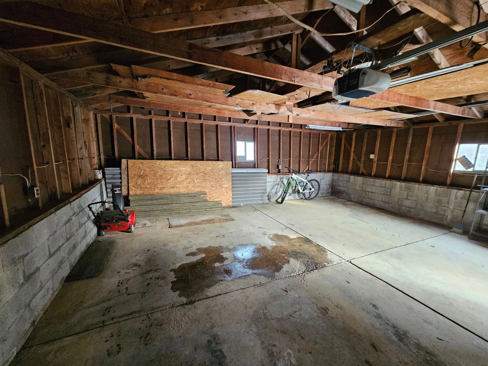 Interior of a garage, with a concrete floor, exposed wooden beams and a motorcycle.