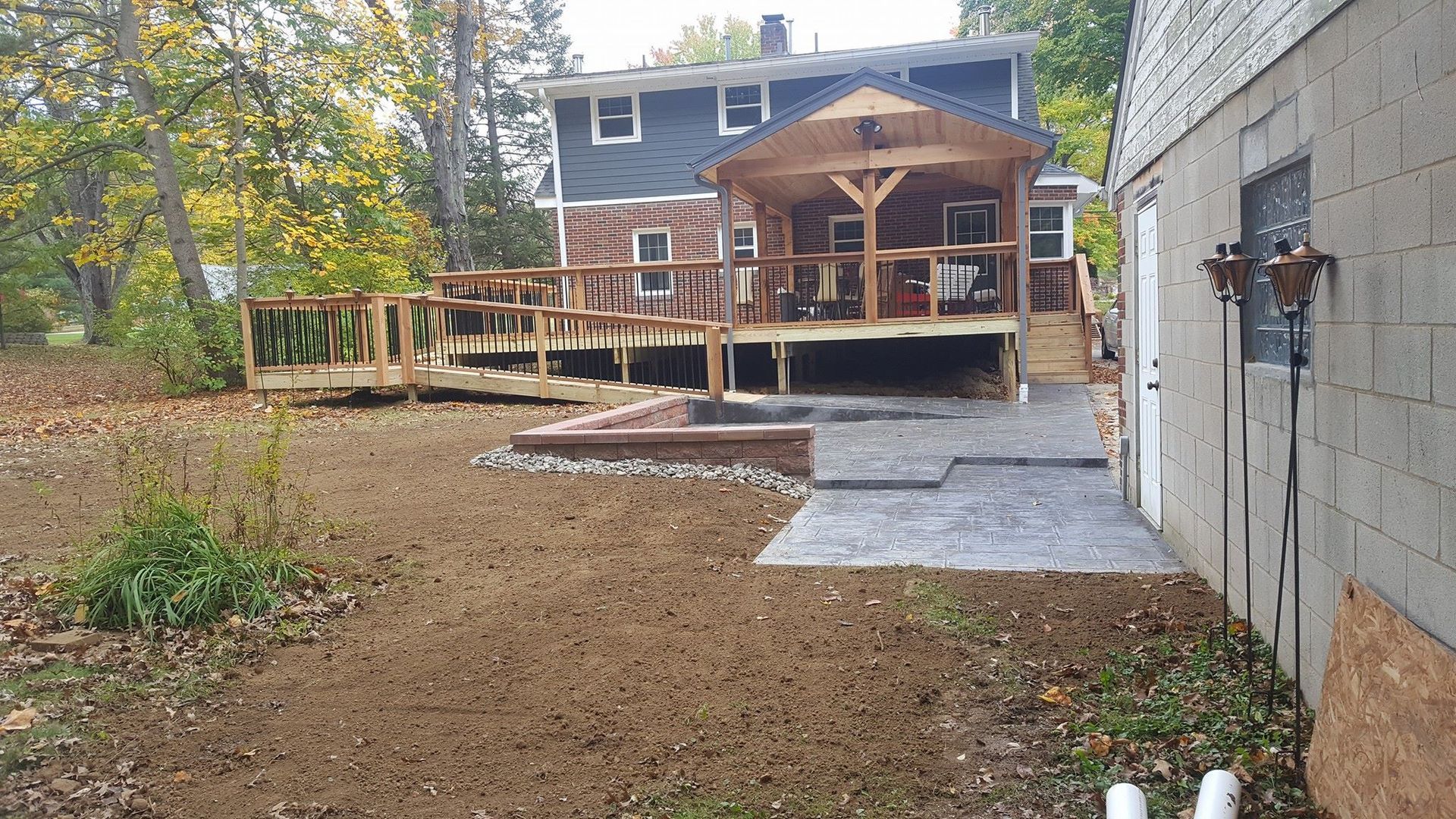 Backyard with deck, patio, and raised flower bed; house in background, leaves on ground.