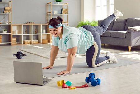 A woman is doing exercises on a yoga mat in front of a laptop computer.