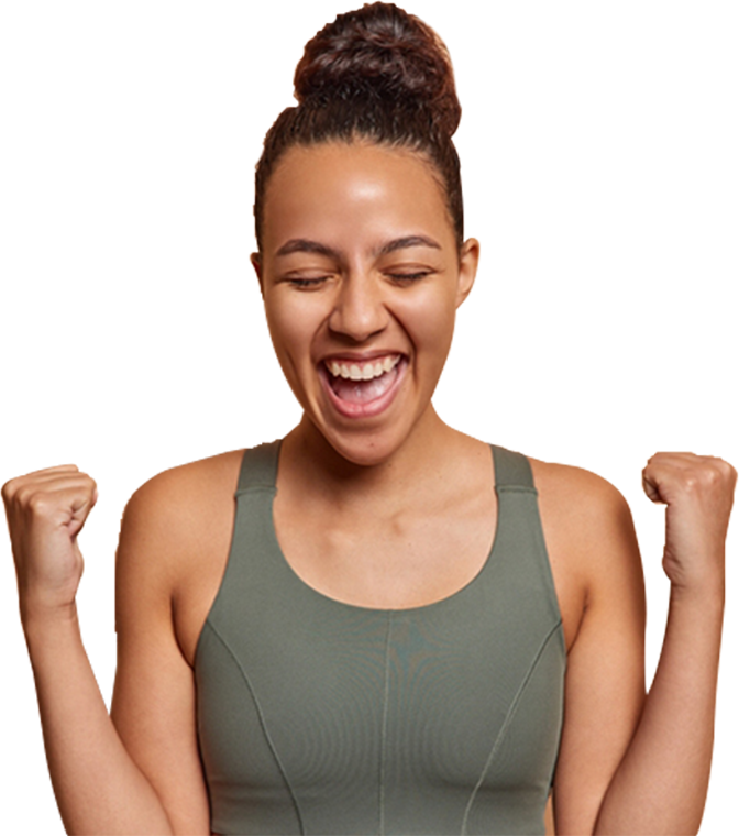 A woman in a green sports bra is smiling with her fist in the air