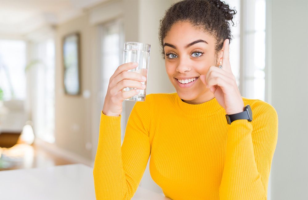 A woman in a yellow sweater is holding a glass of water and smiling.