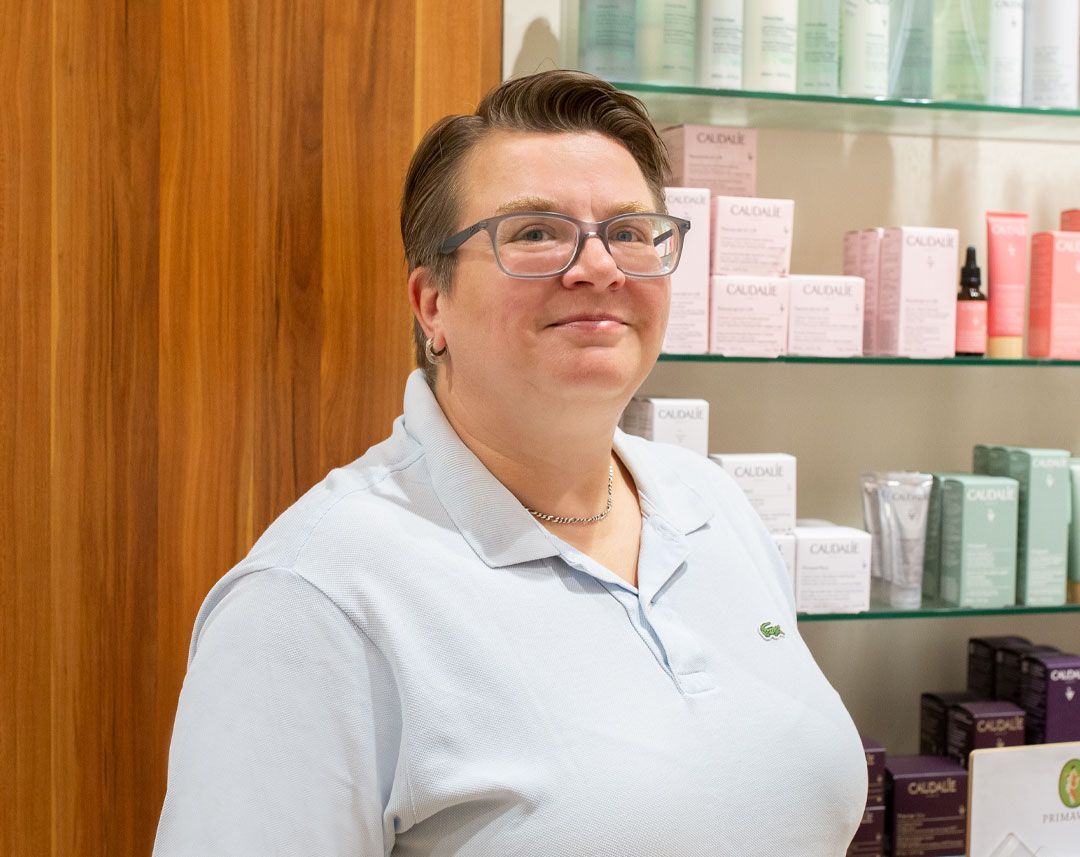 Eine Frau mit Brille steht vor einem Regal mit Kosmetika.