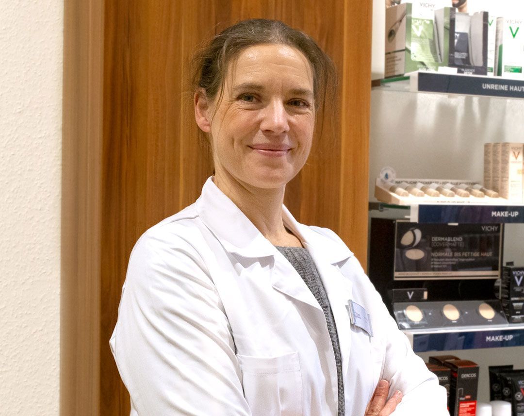 Eine Frau in einem weißen Laborkittel steht mit verschränkten Armen