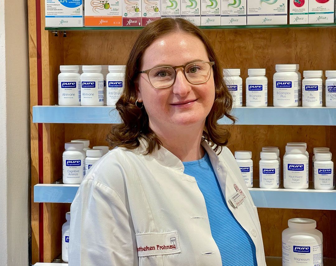 Eine Frau im Laborkittel steht vor einem Regal mit Pillen.