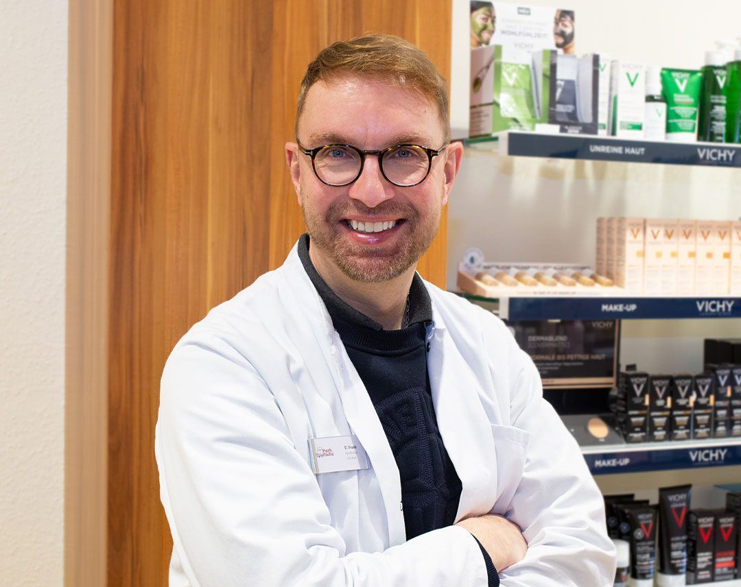 Ein Mann im weißen Kittel und mit Brille steht vor einem Regal mit Vichy-Produkten.