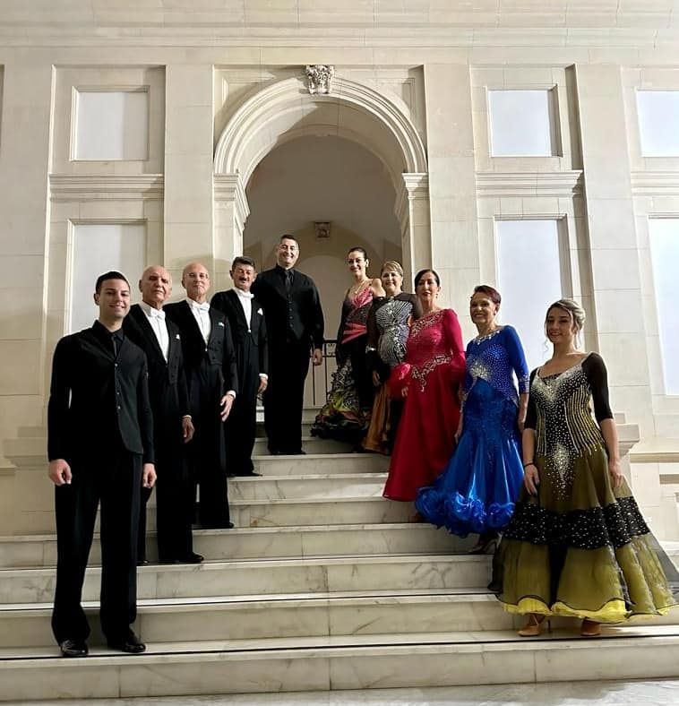 Un gruppo di ballerini in abiti formali posa su una scalinata di marmo sotto una porta ad arco.