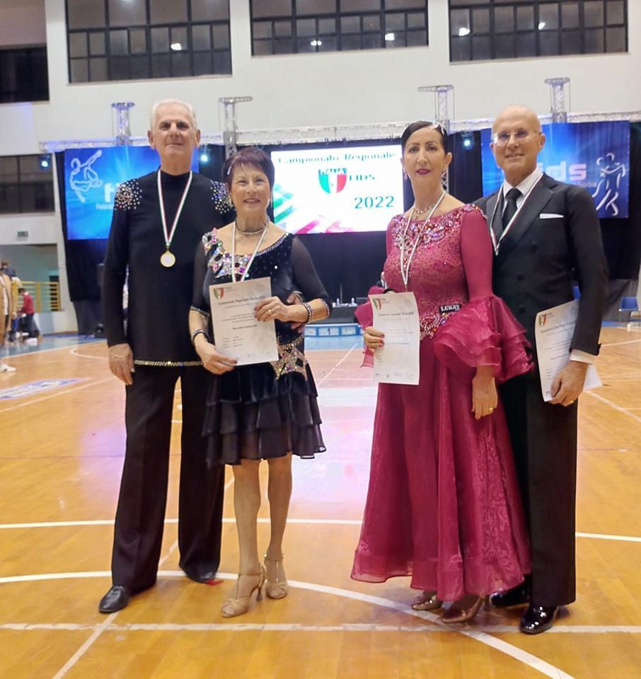 Quattro ballerini di sala, due coppie, posano con attestati e medaglie durante una gara di ballo, al chiuso, 2022.
