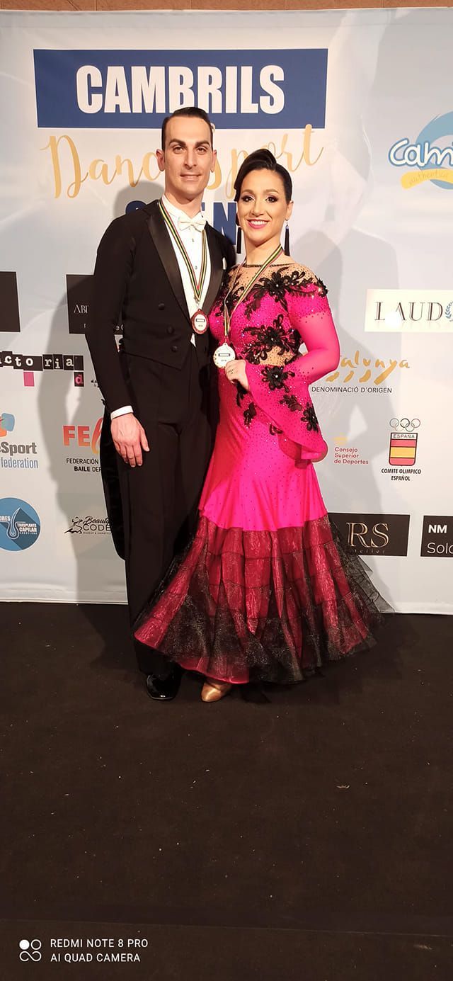 Una coppia in abito formale posa a una gara di ballo. La donna indossa un abito rosa, l'uomo uno smoking.