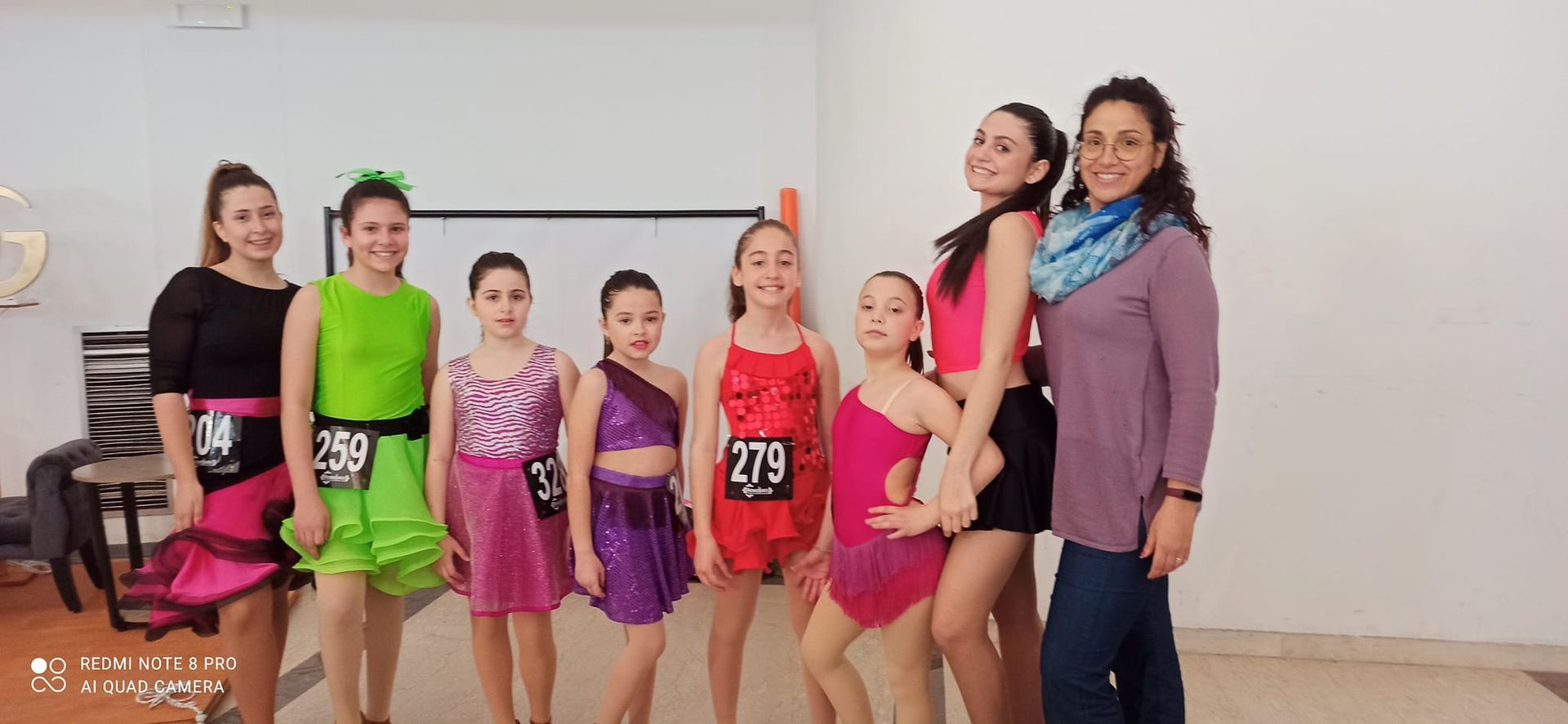 Un gruppo di ballerini in costumi colorati posa per una foto davanti a un muro bianco.