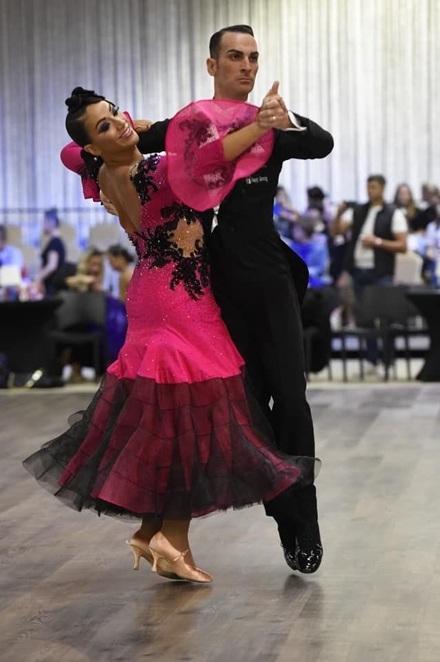 Una coppia in abiti da ballo formali, la donna in abito rosa e nero, l'uomo in abito nero, ballano in una sala da ballo.