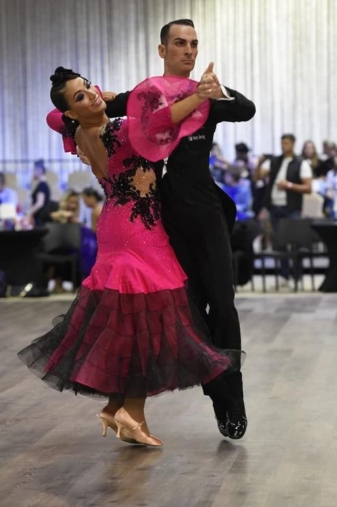 Una coppia in abiti da ballo formali si esibisce, la donna in abito rosa, l'uomo in abito nero, all'interno della sala da ballo.