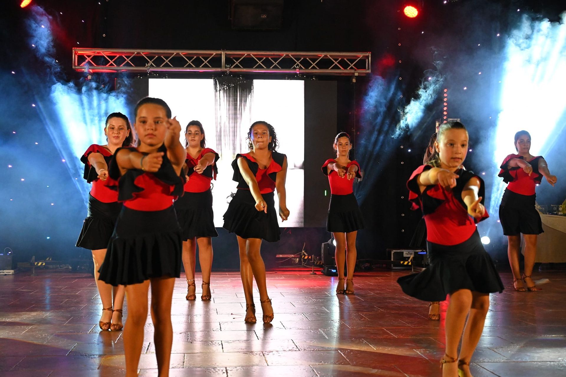 Gruppo di giovani ballerini in abiti rossi e neri che si esibiscono sul palco.