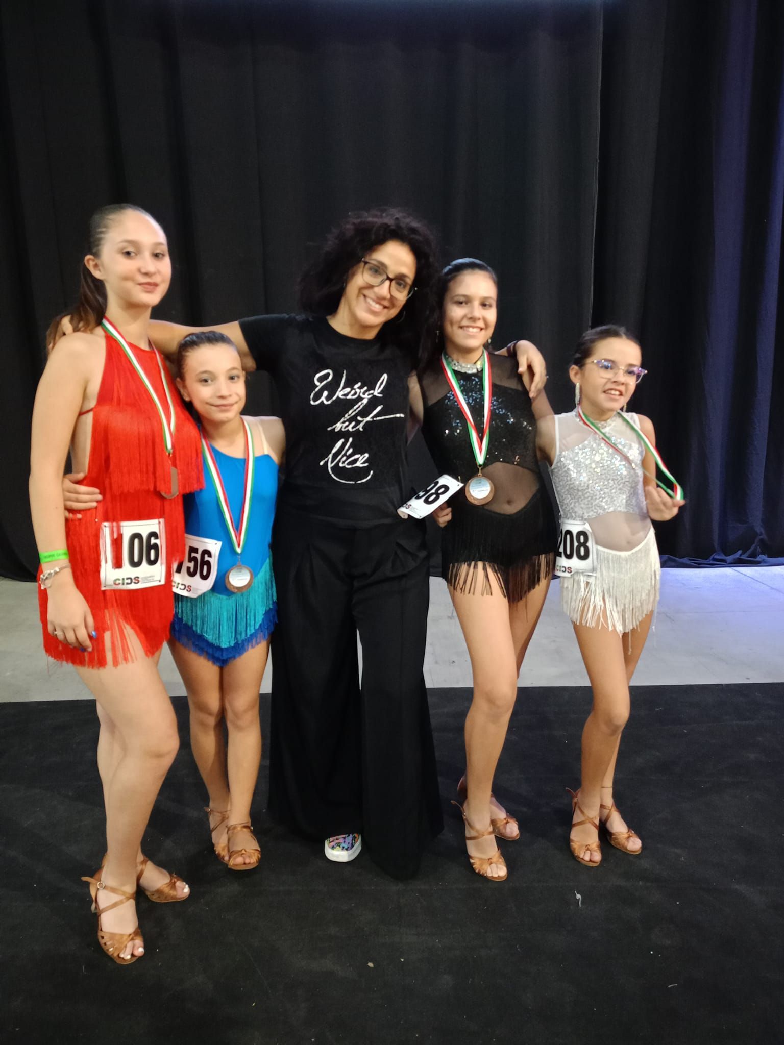 Un gruppo di ballerini e un allenatore con medaglie, in posa, su una pista da ballo.