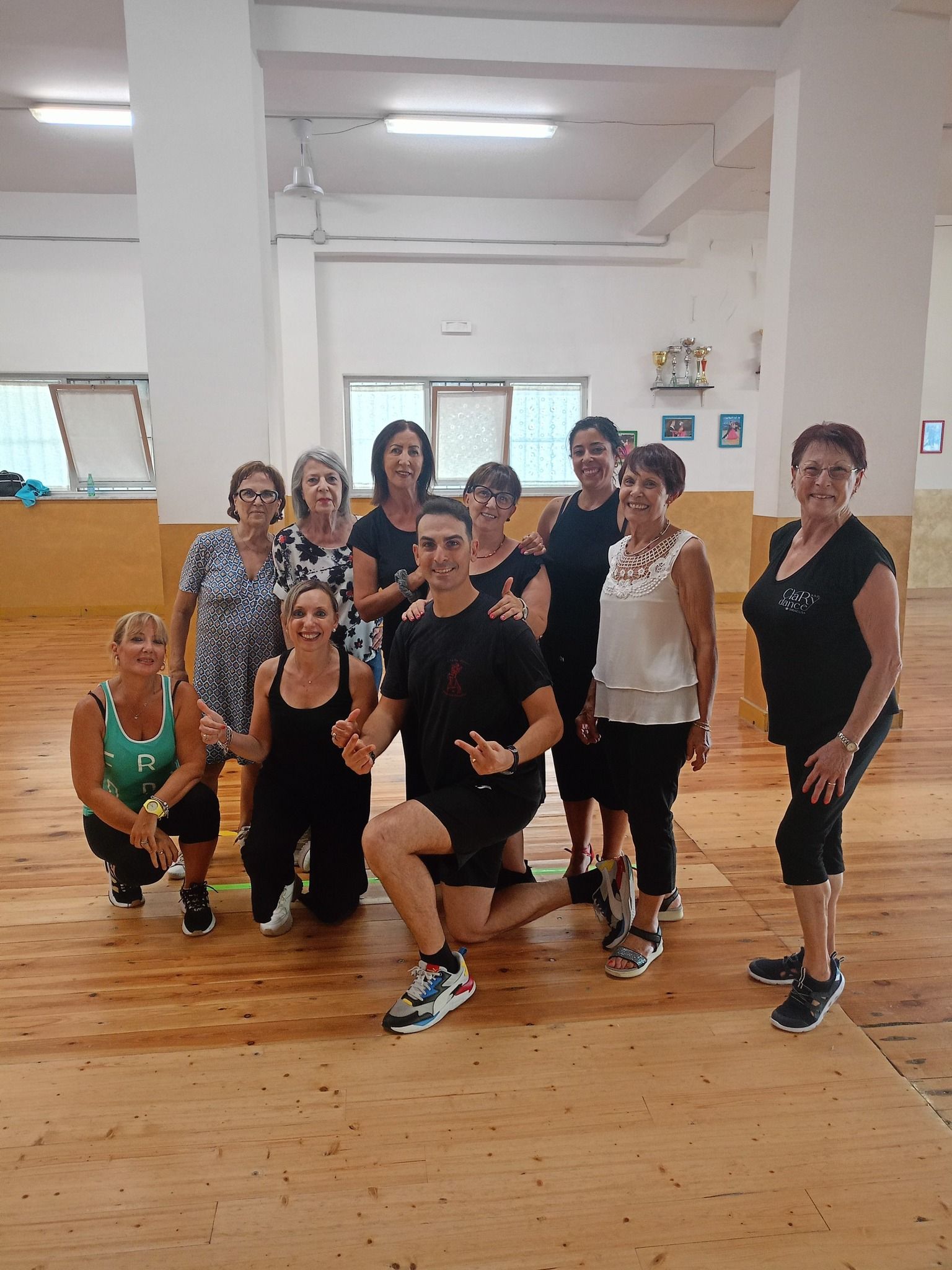 Un gruppo di persone in una sala da ballo posa per una foto con un uomo al centro, tutti sorridenti.