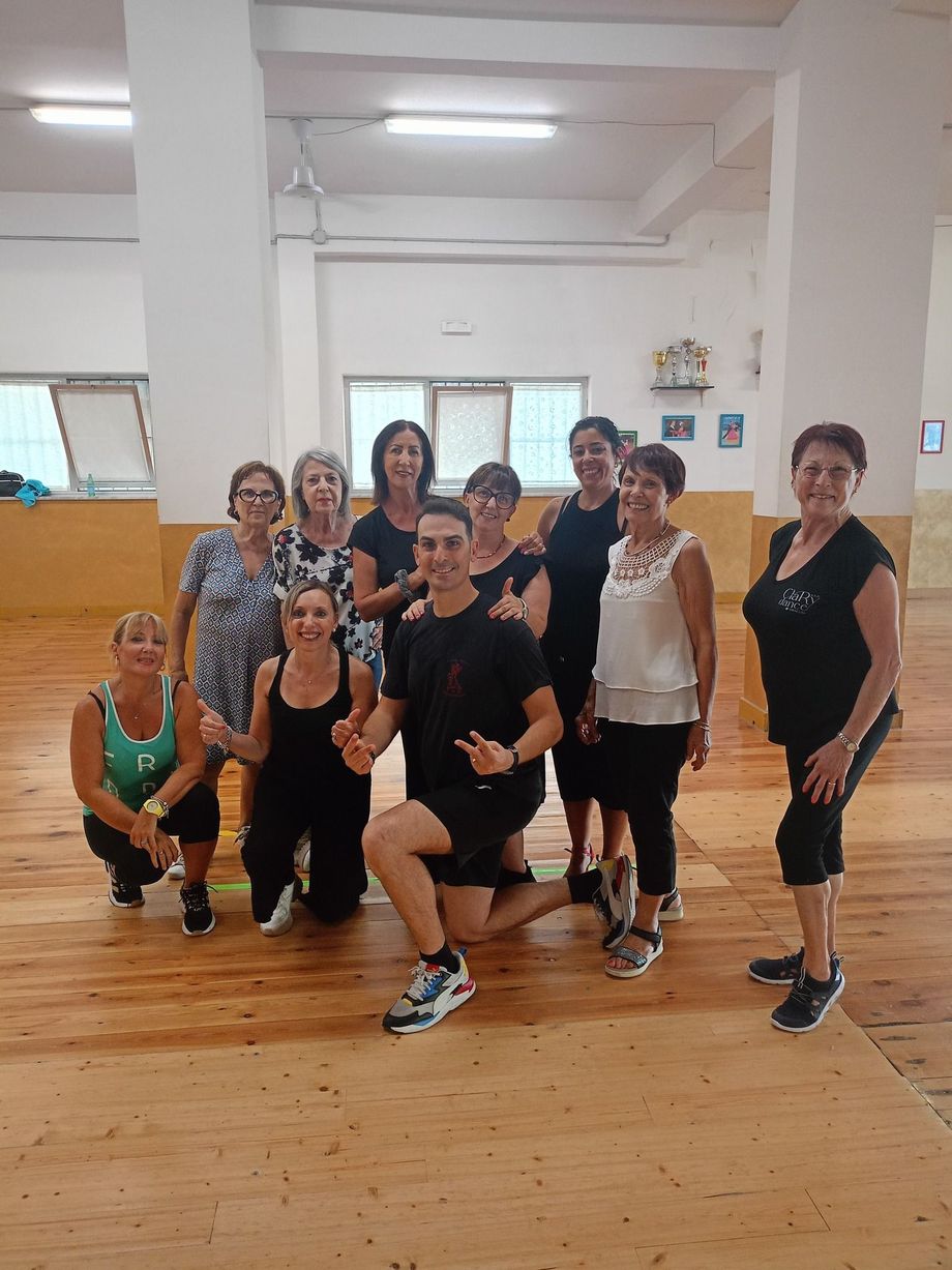 Un gruppo di persone, per lo più donne, posa con un uomo in una scuola di danza. Sorridono.