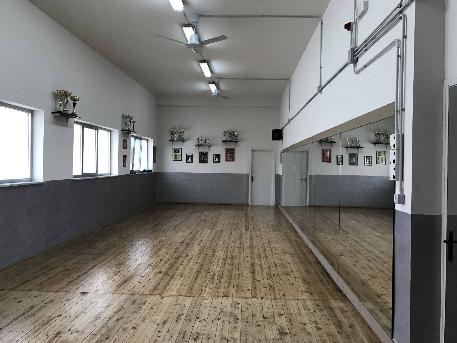 Studio di danza vuoto con pavimento in legno, specchi e finestre.