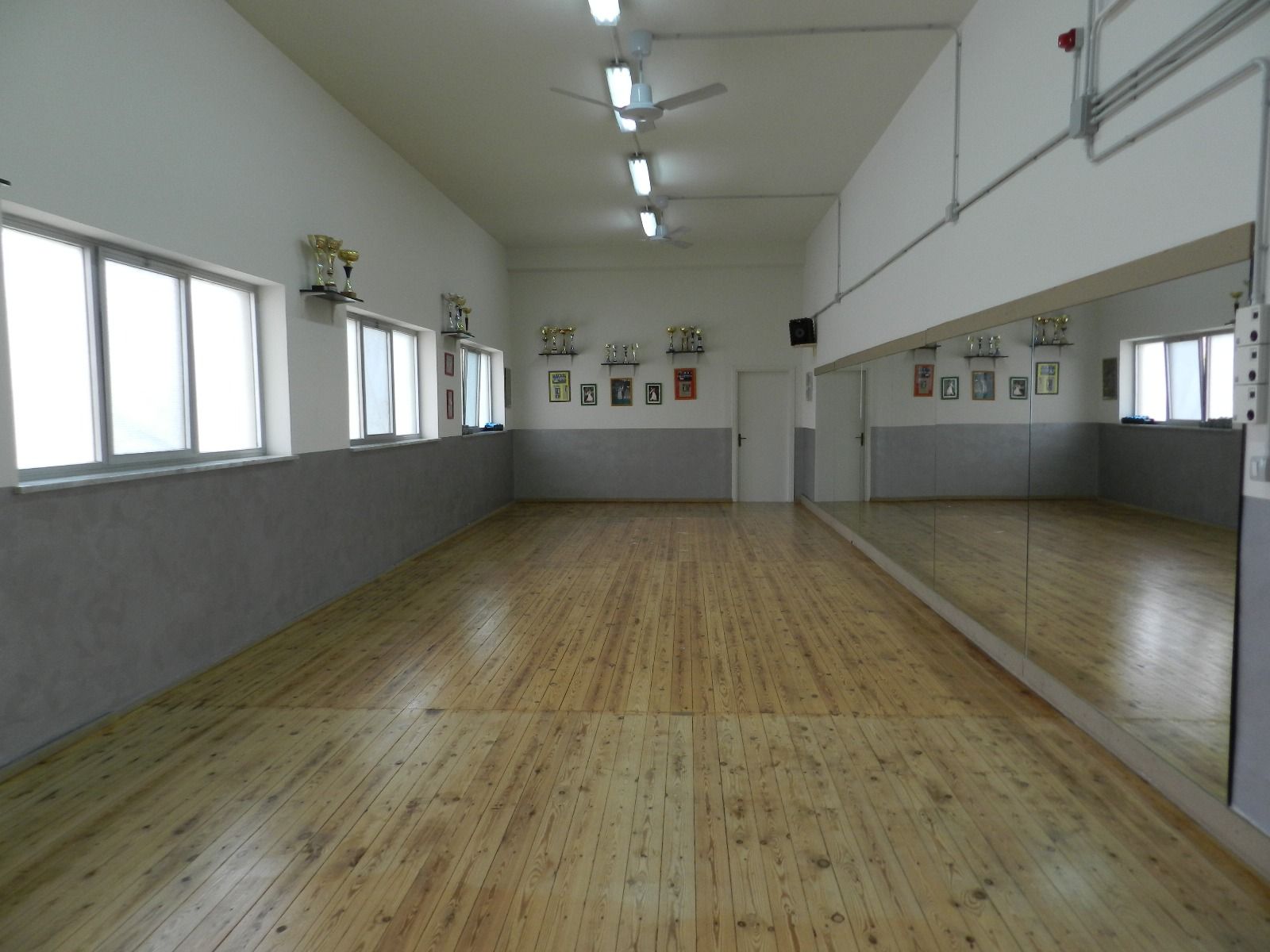 Studio di danza vuoto con pavimento in legno, specchi e finestre.